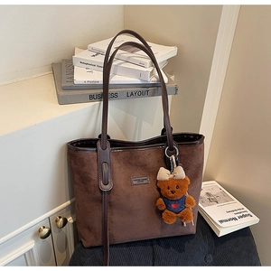 Detail of dark brown suede tote bag featuring a leather logo tag and a cute bear charm
