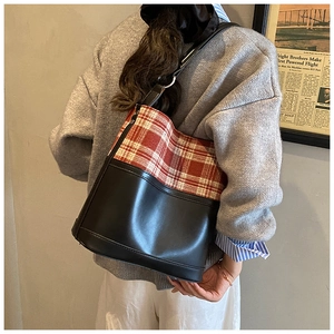 Detail of vintage red checkered and black leather bucket bag worn on shoulder