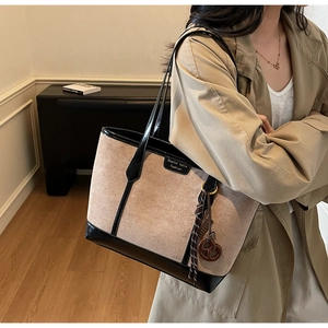 Dettaglio della borsa tote beige in scamosciato con bordi neri e ciondolo vintage