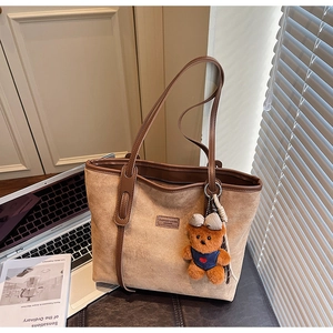 Detail of light brown faux suede tote bag with leather trim and plush bear charm
