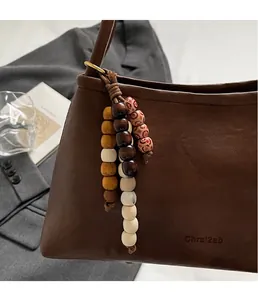 Detail of dark brown leather shoulder bag with decorative wooden beads on grey suit jacket