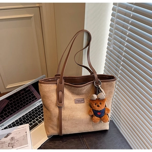 Brown suede tote bag with leather straps and cute bear charm in a lifestyle office setting