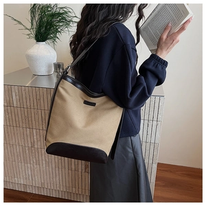 Detail of large canvas tote bag with brown leather trim worn by a model in a minimal setting