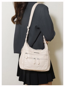 Detailed view of cream soft leather hobo bag with three front zipper pockets on model