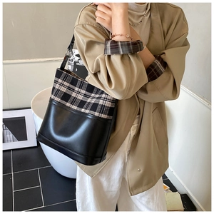 Detail of checkered bucket bag worn crossbody featuring black leather stitching