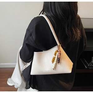 Detail view of white pebbled leather triangle shoulder bag with brand logo and beaded charm