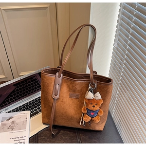 Detail of dark brown suede tote bag with plush bear charm in a lifestyle office setting