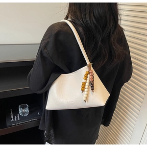 Detail of off-white leather underarm bag with bohemian colored beads and chic texture