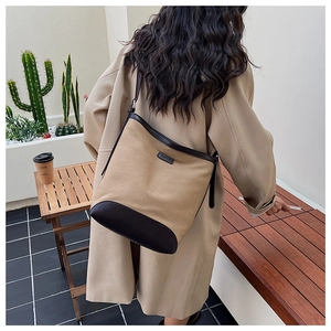 Detail view of khaki canvas bucket bag with brown leather trim worn by model on shoulder
