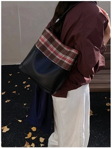 Close-up of the vintage British plaid and black leather tote bag in an autumn street setting