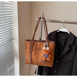 Close-up of brown suede tote bag with leather handles and cute bear charm detail