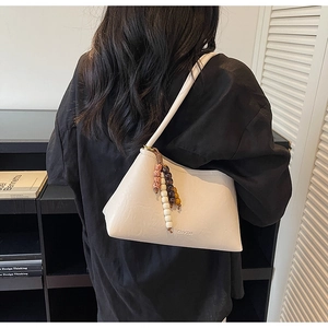 Detail of cream-colored leather baguette bag with ethnic beaded charm and brand text