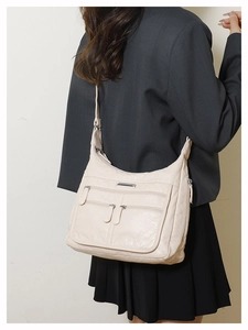Detail of soft cream leather crossbody bag featuring multiple front zipper pockets