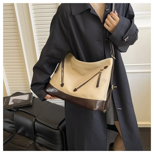 Detail of beige canvas shoulder bag with brown leather base and dual zipper accents