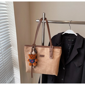 Detail view of large brown suede tote bag with leather handles and bear pendant decoration