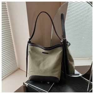 Detailed macro view of olive canvas bucket bag with brown leather trim and metal logo