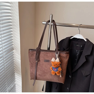 Detail view of brown suede tote bag with a teddy bear charm and metal fashion logo