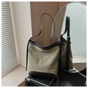 Detailed close-up of green canvas tote bag with brown leather trim and metal buckles