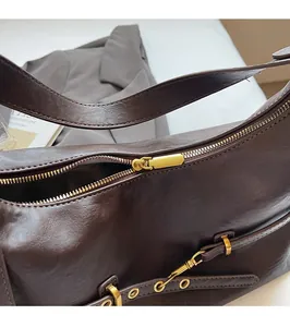 Dettaglio della cerniera dorata e fibbia del cinturino su borsa sottobraccio marrone scuro