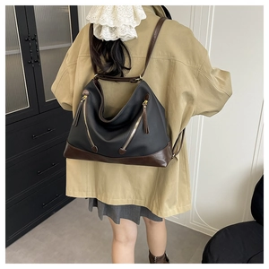 Detail of a large two-tone tote bag with gold zippers worn on a model's shoulder