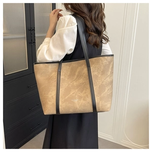 Detail of light brown tote bag with black leather straps and brand logo on a modern setup