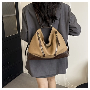 Detail of khaki canvas and brown leather bucket bag showing dual zipper pockets and strap
