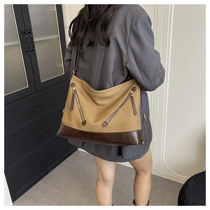 Detailed side view of large canvas tote bag with brown leather patchwork and zippers