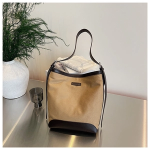 Detail of canvas and leather bucket bag with contrast trim on a minimalist metal surface