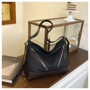 Close-up of contrast leather tote with dual gold zippers on a rustic wooden table