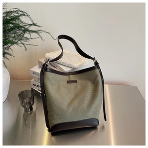 Detail of army green canvas bucket bag featuring dark brown leather trim and logo patch
