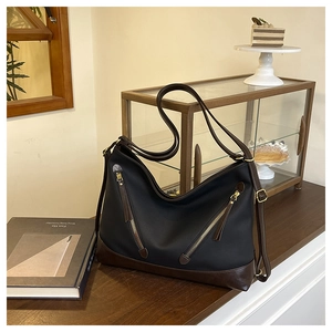 Detail of black pebbled leather bucket bag with brown straps and golden zippers