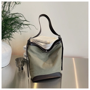 Detail of army green canvas hobo bag with dark brown leather trim on a metal table