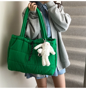 Close-up of a green quilted tote bag with soft texture and white plush rabbit charm