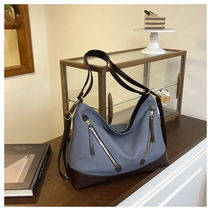 Detail of blue canvas bucket bag with brown leather trim and metal zipper accents