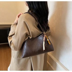 Close-up of a vintage brown leather underarm bag with beaded charm and embossed detail
