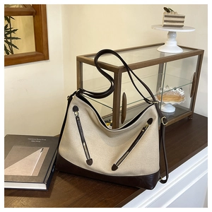 Detail view of large canvas tote bag with diagonal zippers and brown leather trim base