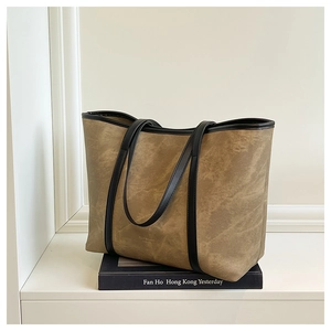 Close-up of brown textured leather tote bag showing black piping and premium stitching