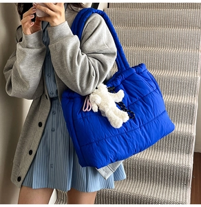 Detail view of quilted puffer tote bag in royal blue with fluffy bear charm on model