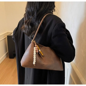 Detail view of brown vintage shoulder bag with bohemian bead charm and thin strap