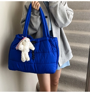 Detail of blue quilted tote bag featuring a white plush rabbit charm and drawstring closure