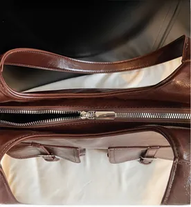 Detail of a dark brown leather tote bag with a smooth metal zipper and premium finish