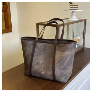 Detailed texture of retro taupe tote bag featuring dark brown leather handles and branding