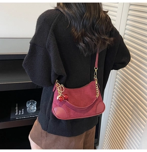 Detail of burgundy suede shoulder bag with gold chain strap and cherry pendant charm