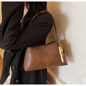 Detail of vintage brown leather shoulder bag featuring a unique beaded charm accessory