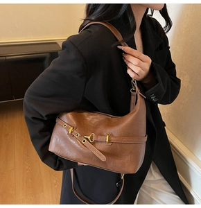 Dettaglio borsa hobo in pelle marrone con fibbia dorata indossata da modella in nero