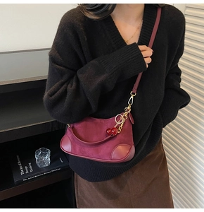 Detail of burgundy suede hobo bag with gold chain and cherry charm on model