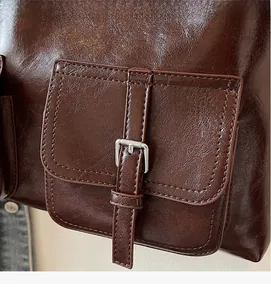 Detail of dark brown leather tote bag with silver buckle and glossy oil skin finish