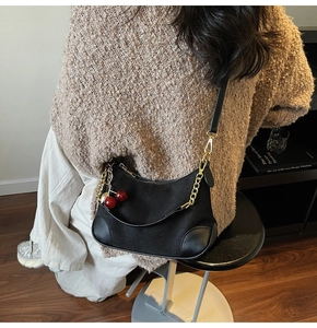 Detail van zwarte suède hobo tas met gouden ketting en rode kersenhanger op schouder