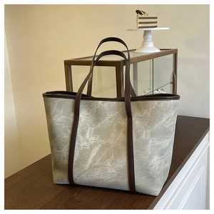 Detailed shot of marble-patterned tote bag with brown leather handles on wooden surface