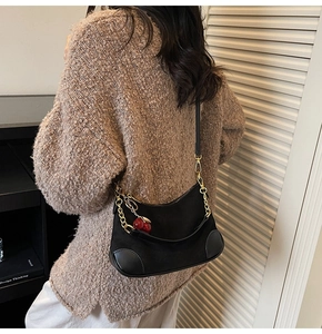 Detail of black baguette bag with gold chain and red cherry charm on knit sweater